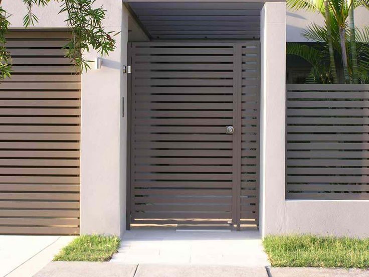 Portail aluminium contemporain avec barreaux horizontaux de couleur marron claire. Entrée avec mur blanc et multitude de palmiers.