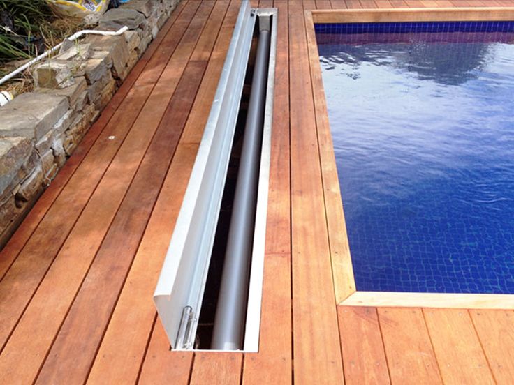 Aménagement d'une piscine rectangulaire classique avec bois et mosaïque bleue. Système pour dérouler bâche et petit muret de pierres à proximité.