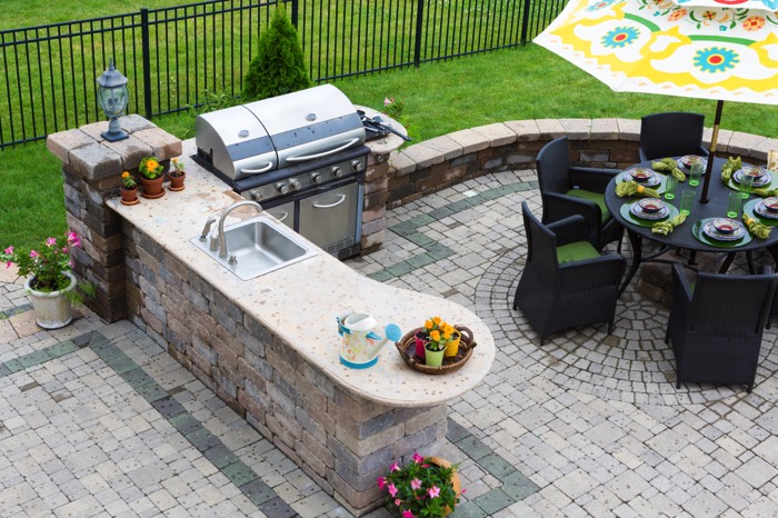 Pavés roses et gris pour une terrasse contemporaine accueillant un plan de cuisine, un barbecue et une table ronde de jardin