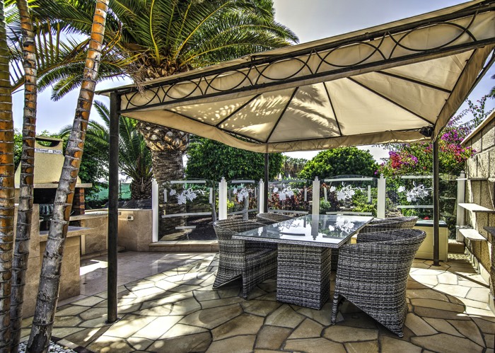 Tente d'été avec table de repas d'extérieur en rotin à côté d'une jolie cuisine d'été en pierre et son barbecue