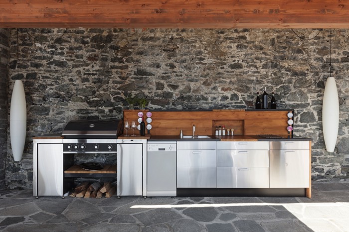 Aménagement d'une cuisine en inox ouverte sur le jardin. Mur en pierre avec lampes suspendues modernes