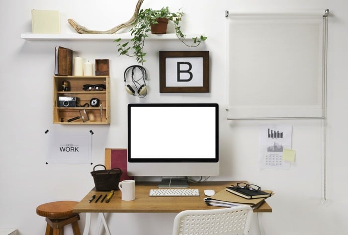 Aménagement d'un petit bureau en bois chêne avec chaise blanche. PC moderne, pièce blanche, petite étagère, tableau blanc, plantes et divers objets.