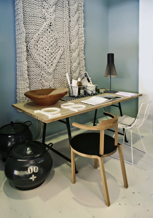 Aménager un petit bureau en bois hêtre avec chaises en bois et blanche. Pièce avec sol uni en beige, mur vert clair et grands pots noirs.