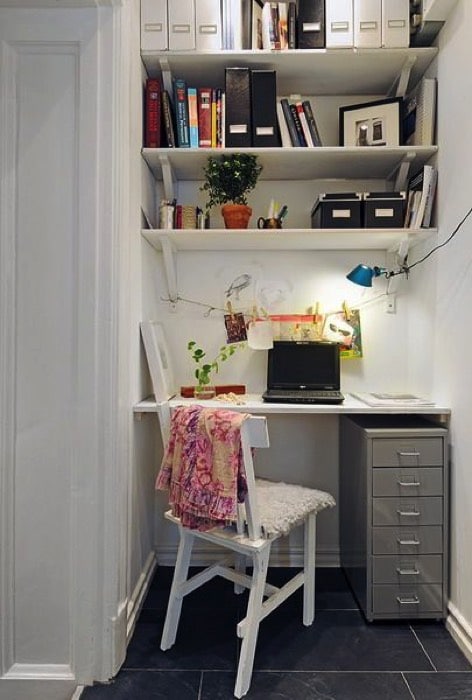Aménager un petit bureau blanc avec un PC portable noir dessus. Étagères avec différents classeurs, livres et tiroirs gris sur carrelage.