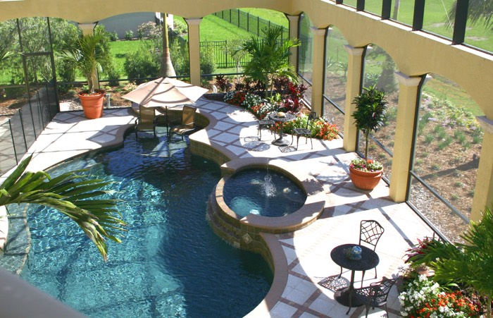 Aménagement d'une terrasse zen avec piscine arrondie multiforme dotée d'une belle fontaine. Parasol blanc, plantes et grande verrière autour.