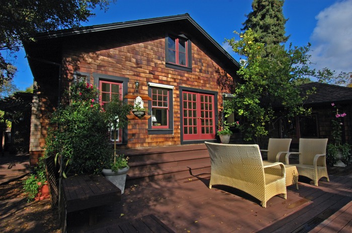 Terrasse zen classique avec parquet en bois wengé, arbres et végétation. Maison en pierres et salon extérieur blanc-beige.