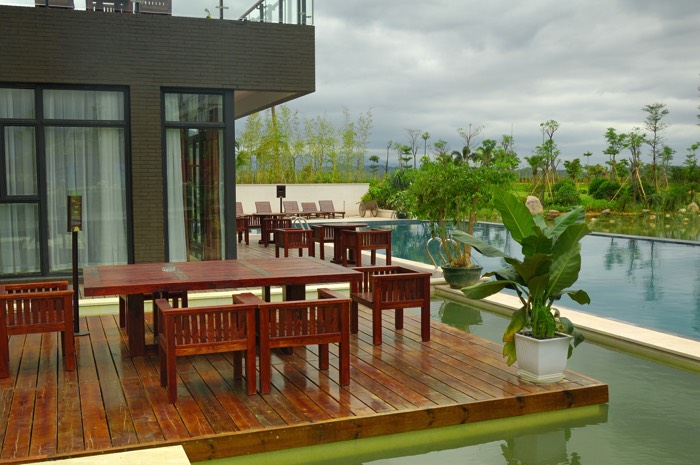 Aménager une terrasse zen avec salon extérieur en bois et parquet. Maison moderne architectural avec grande piscine rectangulaire et végétation à proximité.