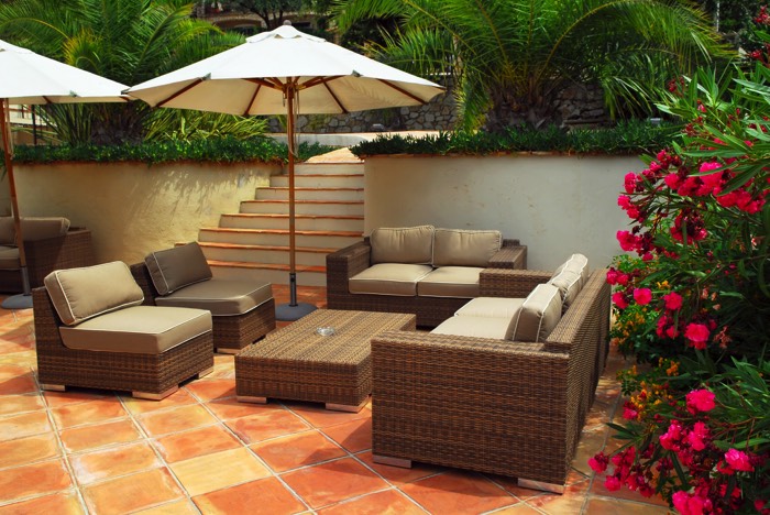Aménagement d'une terrasse zen avec carrelage orange et parasol blanc. Salon extérieur avec fauteuils et table basse tressée au milieu de végétation.