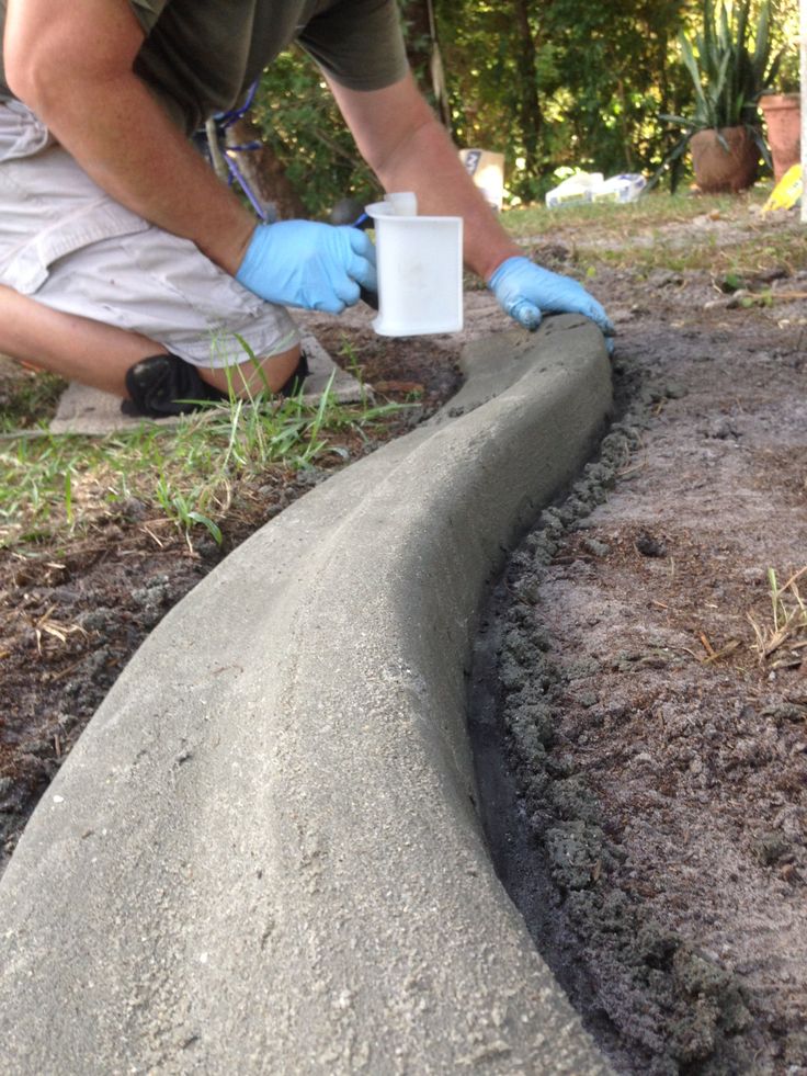 Préparation d'une pose d'une bordure béton classique de forme arrondie qui servira de délimitation entre une pelouse et un espace jardin.