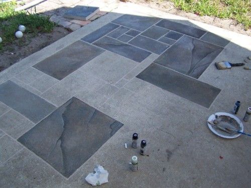 Passer la première couche de peinture pour peindre une terrasse en vieux gris en belles nuances de gris. Matériel de peinture et pelouse à proximité.