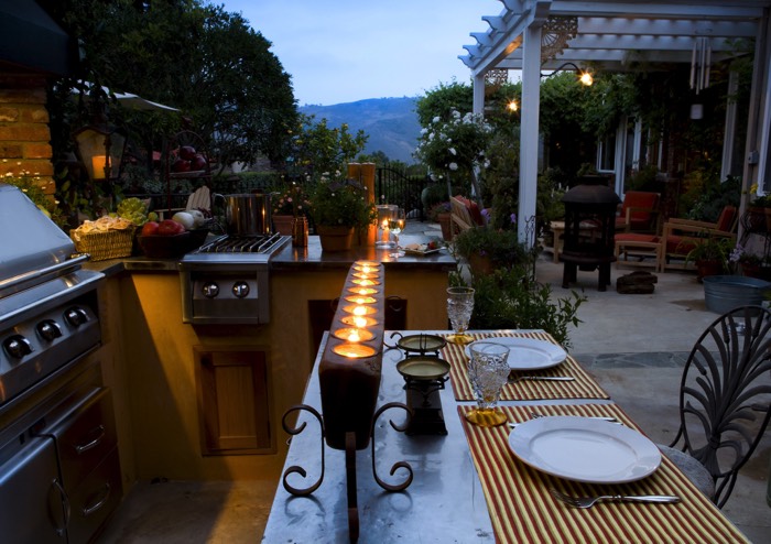 Cuisine d'été de charme avec la présence de l'inox et du fer forgé. Pergola blanche jouxtant la terrasse en marbre et ardoise.