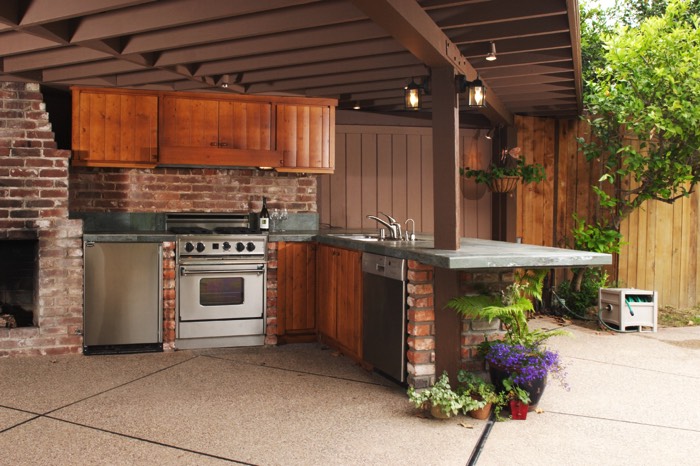 Pergola en aluminium au dessus d'une cuisine de jardin avec son plan en béton ciré et ses équipements en inox.