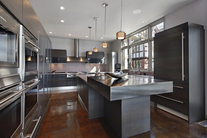 Cuisine gris anthracite avec îlot central sur parquet stratifié. Lampes suspendues, spots au plafond, grande fenêtre et hotte en acier.