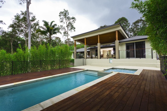 Piscine en bois teck de forme rectangulaire allongée avec dalles autour et petit escalier. Jacuzzi dans le même style que la piscine juste à côté.