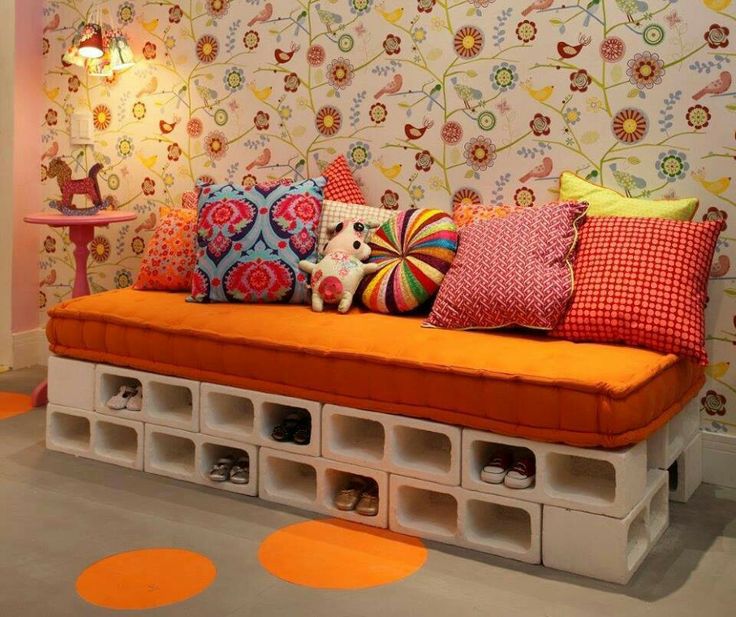 Parpaings décoratifs servant de meubles à chaussures mais aussi de piliers pour le matelas, formant un canapé orange. Magnifique tapisserie blanche avec oiseaux et fleurs multicolores.