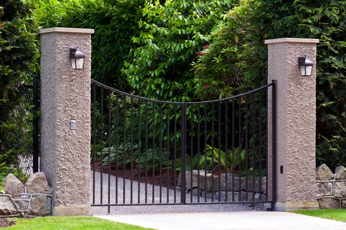 Entrée portail avec deux colonnes et deux petites lampes accrochées ainsi qu'une allée gravillonnée avec pelouse. Petit portail à double battants.