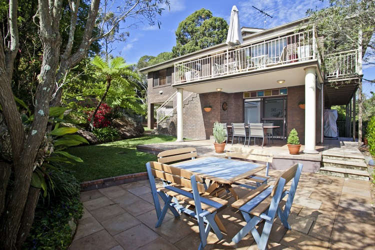 Aménagement d'un extérieur maison avec petit salon en bois bleu. Maison à étages blanche à pierres avec jardin moderne zen doté d'une belle pelouse.
