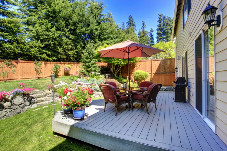Aménager un extérieur maison avec terrasse dotée d'un parquet blanc. Baies vitrées donnant sur un magnifique jardin avec sapins, pelouse et fleurs.