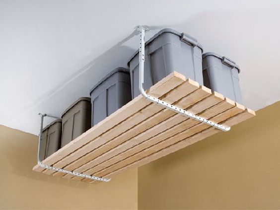 Idée de rangement originale et pratique avec du parquet suspendu en hauteur sur plafond blanc. Mur beige et grands contenants gris sur le parquet.
