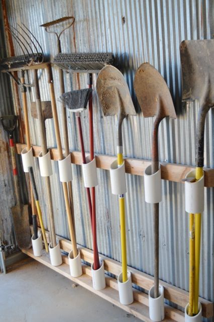 Idées de rangements utile pour différents outils de bricolage comme des pelles ou des fourches. Tubes blancs fixés à des planches en bois pour maintenir les outils.