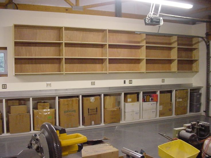 Idée d'un grand rangement en bois avec 15 cases ouvertes rectangulaires identiques vides. Mur uni blanc-beige et sol gris.