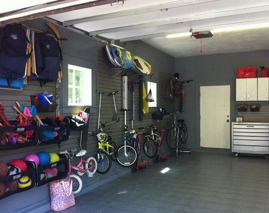 Idées rangements pour un garage gris avec carrelage servant à suspendre des vélos, des trottinettes, des casques de différentes couleurs ou encore un skateboard.
