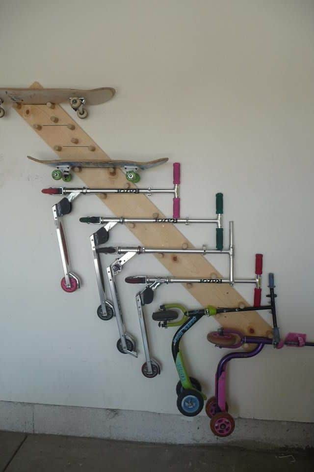 Idée d'un rangement utile en bois sur mur uni blanc. Multitude de skates et de trottinettes de différentes couleurs, allant du rose au vert.