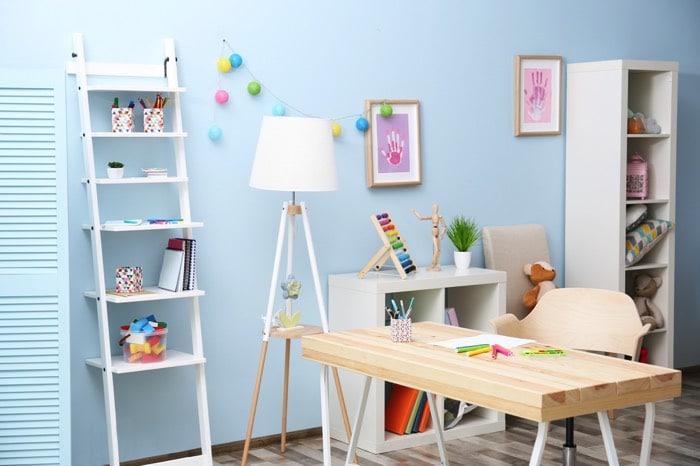 Aménagement d'un bureau rectangulaire en bois orme sur parquet. Mur uni bleu avec décoration pop pour enfants, tableaux roses et jouets.