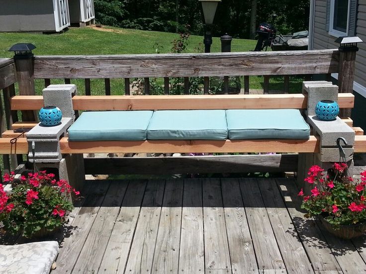 Parpaing décoratif servant d'accoudoirs à un banc extérieur fait de palettes et avec des coussins en bleu clair. Parquet extérieur avec vue sur pelouse et jardin.