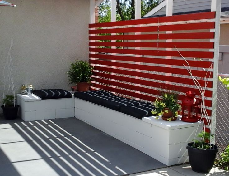 Parpaings décoratifs tout en blanc formant un banc extérieur en L comportant des plantes et des coussins en bleu-gris foncé.Parpaing décoratif formant un banc extérieur comportant des plantes et des coussins
