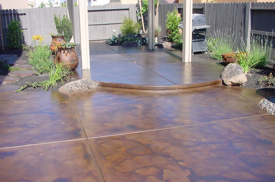 Peindre une terrasse en béton de plusieurs nuances marrons et oranges avec effet terre. Plantes à proximité et clôture en bois.