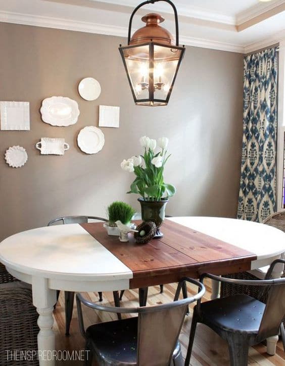 Salle à manger taupe composée d'une table blanche et en bois avec quatre chaises au style industriel. Des plantes harmonisent l'ambiance.