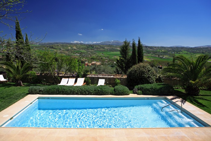 Piscine rectangulaire avec eau bleue et marches. Jardin avec végétation, transats blancs, pelouse et incroyable panorama sur la vallée.