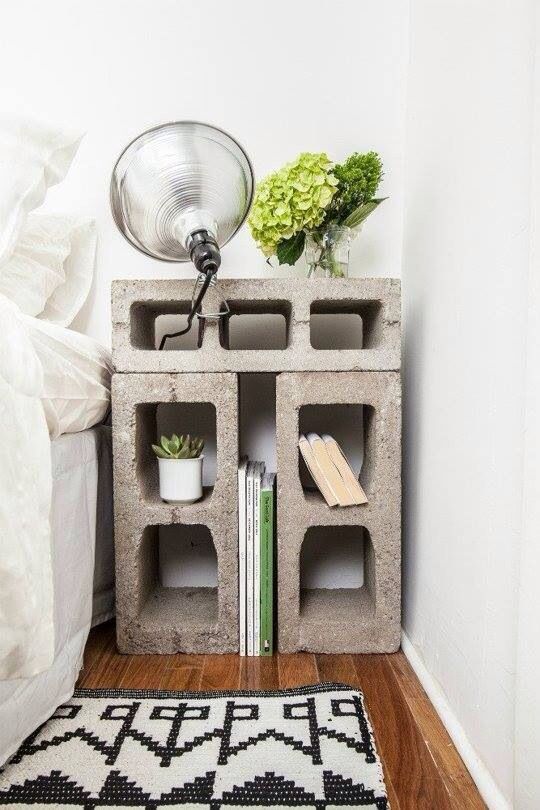 Idée parpaings servant à faire une table de chevet style industriel avec plantes et livres. Tapis blanc et noir style geek sur parquet.
