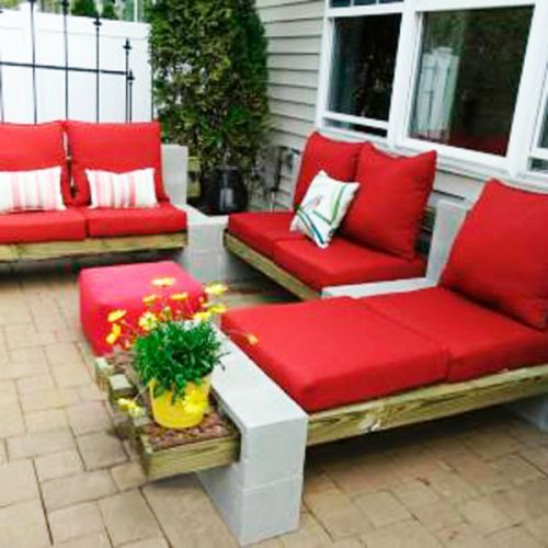 Idée parpaings extérieurs classiques servant de support pour petits canapés en bois avec assises rouges. Terrasse avec carrelage et clôture noire.