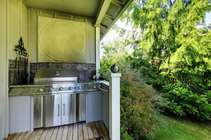 Cuisine d'été ouverte aménagé blanche avec barbecue intégré, carrelage mural en mosaïque, rangement en inox et blanc. Parquet en vieux bois.