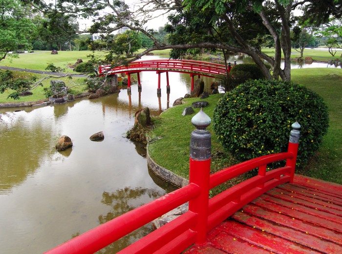 Jardin aménagé comprenant deux ponts en bois de couleur rouge situés au-dessus d'une rivière. Buissons taillés, arbres et pelouse.Jardin aménage comprenant deux ponts en bois de couleur rouge situés au-dessus d'une rivière. Les buissons ont été taillés.