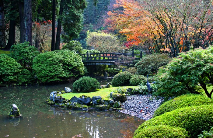 Jardin paysager style japonais zen dans un décor d'automne. Pont en bois au-dessus d'une rivière avec une multitude d'arbres et de buissons différents.