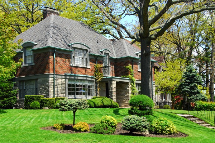 Maison à étages en brique style colonial moderne en briques rouges avec balcon et cheminée. Pelouse, végétation abondante et arbres.