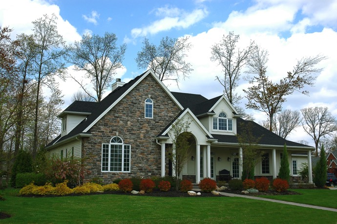 Maison en brique style colonial moderne en pierres avec toiture grise foncée. Petite allée donnant sur une entrée abritée avec pelouse.