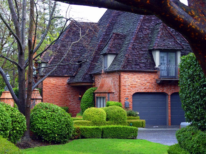 Maison en briques à plusieurs étages style colonial et moderne en pierres rouges avec toiture original en violet foncé. Jardin avec buissons et pelouse.