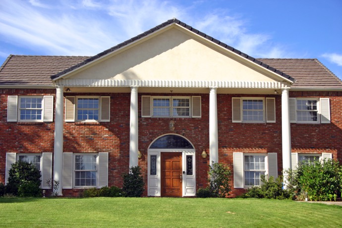 Maison en briques rouges style colonial moderne avec une multitude de fenêtres. Quatre colonnes blanches, porte en bois et magnifique pelouse.