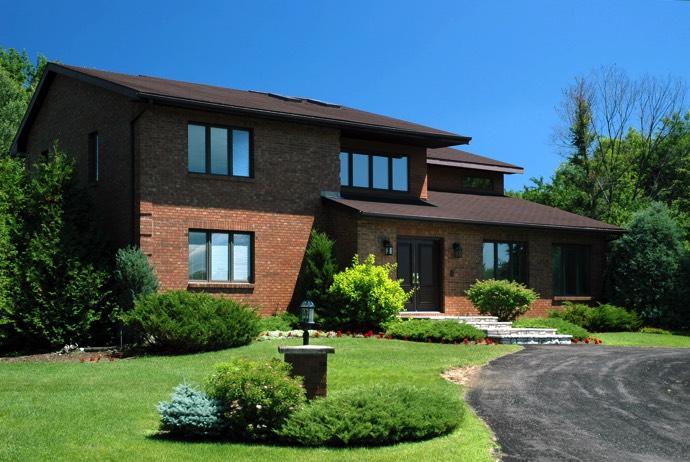 Maison en briques rouges style moderne doté d'un toit marron avec pelouse, plantes et entrée gravillonnée. Pas de porte avec escalier en pierres.
