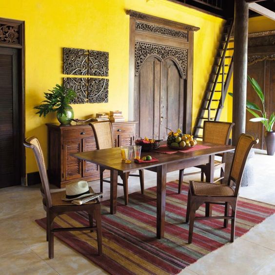 Salle à manger jaune pop or avec table à manger en bois avec quatre chaises sur tapis. Buffet en bois wengé et magnifique porte.