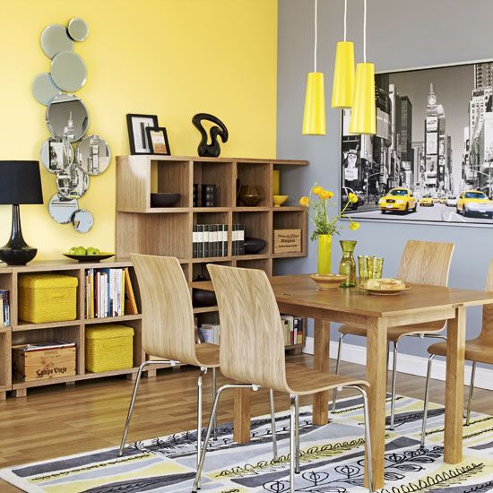 Salle à manger jaune clair pop avec miroirs contemporains et tableau en noir et blanc. Table à manger, chaises et petits rangements en bois.