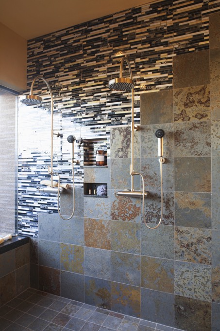 Deux colonnes de douche simples en inox. Douche à l'italienne avec style industriel et carrelage mural en différentes teintes de gris et de marron.