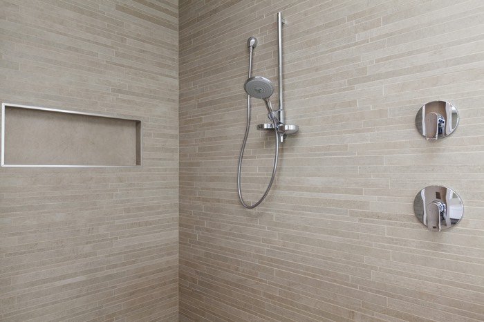 colonne de douche encastrée en inox dans une douche à l'italienne en pierre naturelle