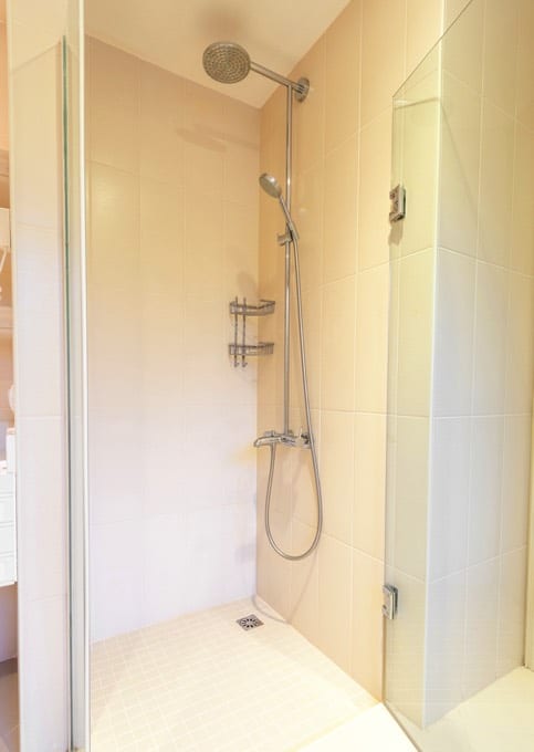 Colonne de douche hydromassante en inox avec pommeau de douche rond. Salle d'eau avec douche blanche et receveur plat.