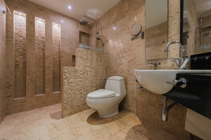 Salle d'eau ambiance ethnique exotique. Douche à l'italienne avec paroi en pierre, colonne de douche hydromassante et pommeau de douche rond.