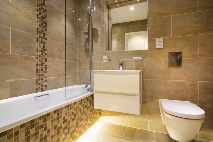 Baignoire blanche avec colonne de douche hydromassante en inox. Salle de bain avec mur orange terre et miroir et petite mosaïque en nuances marron et beige.